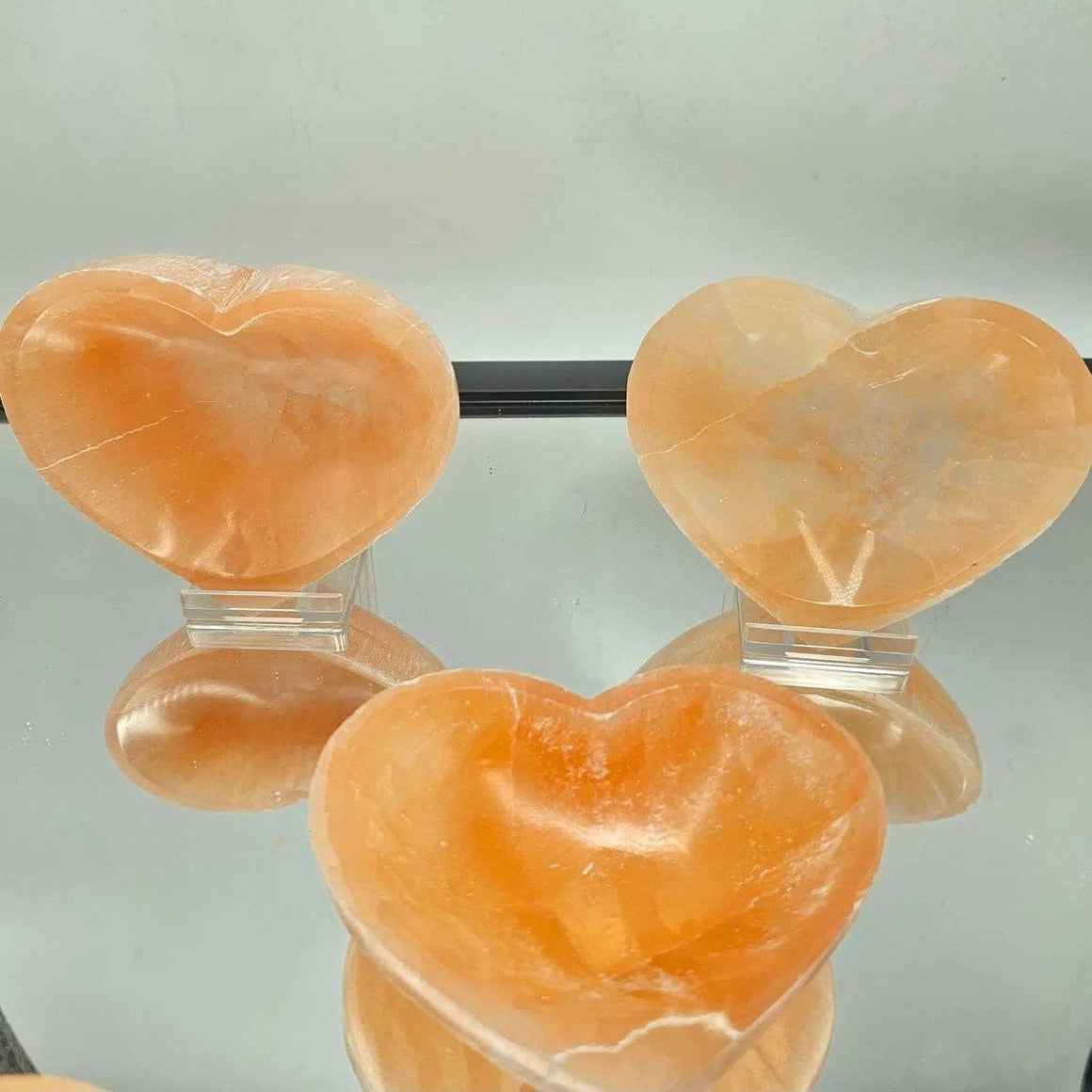 Three heart-shaped orange stones on clear stands against a light gray background