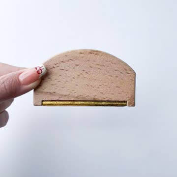 Plastic-Free Travel Lint Remover by Smile Boutiques with wooden handle and metal edge.