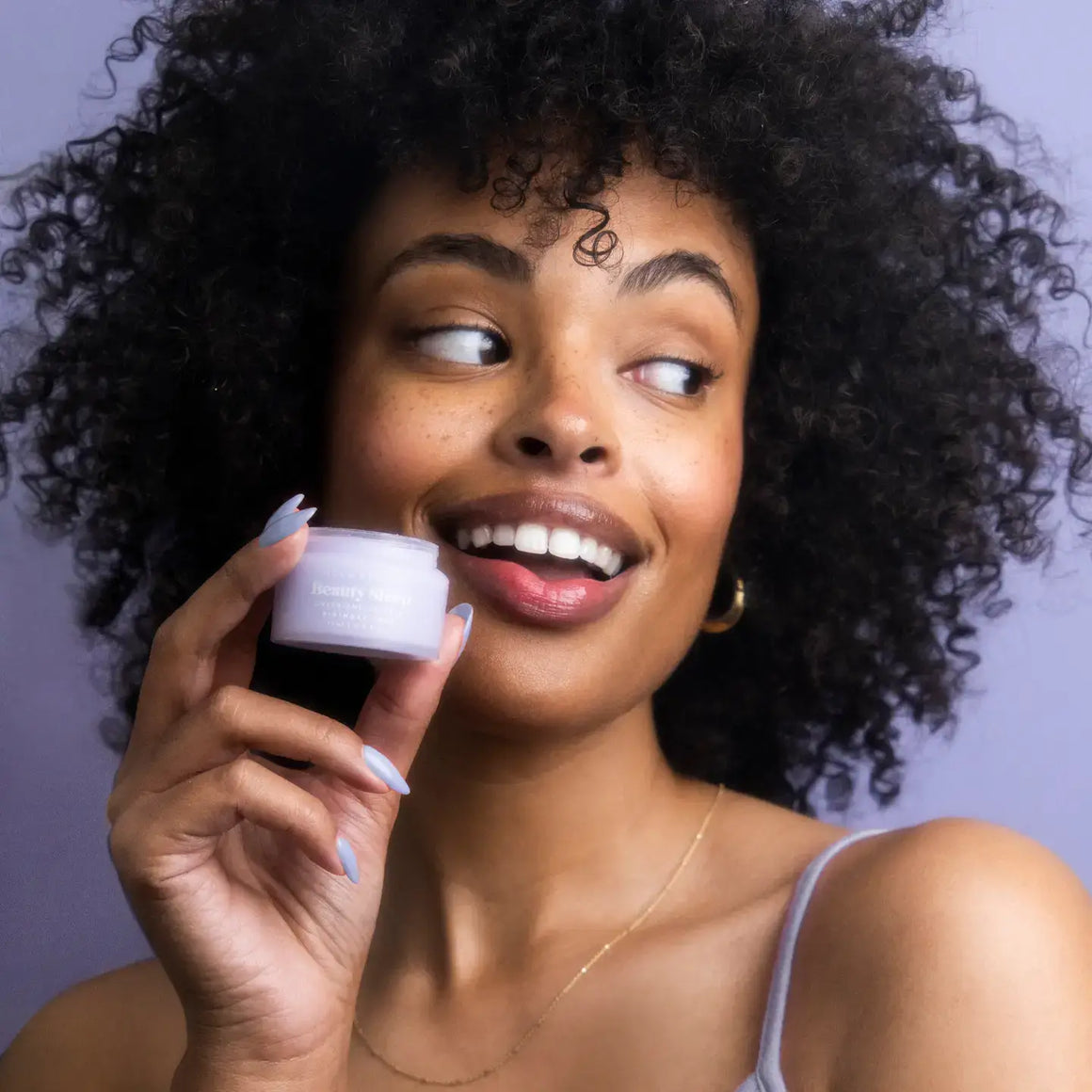 Model holding Beauty Sleep Overnight Lip Mask - Birthday Cake with a joyful expression and beautiful curls.