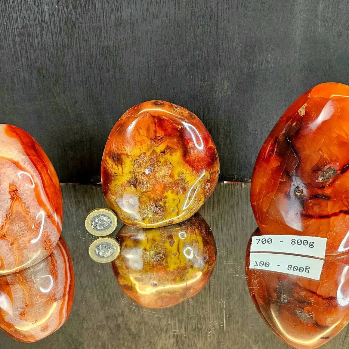 Three polished amber stones on a reflective surface with a dark background