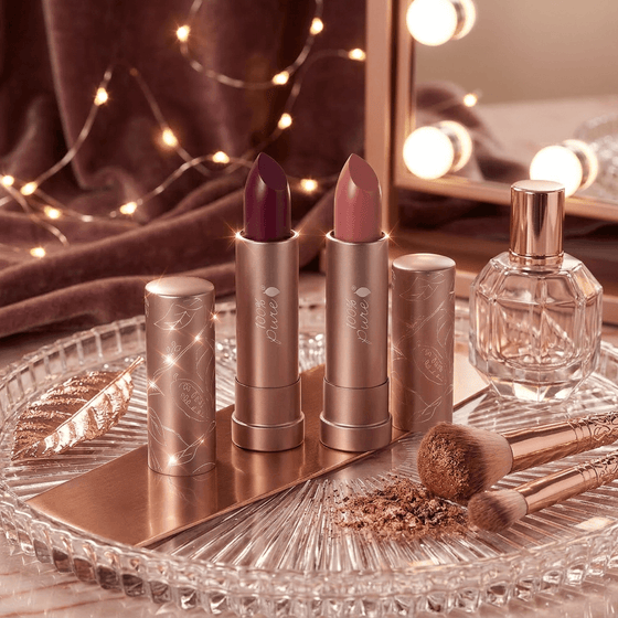 Makeup products including lipsticks, a perfume bottle, and brushes on a decorative tray with warm lighting.